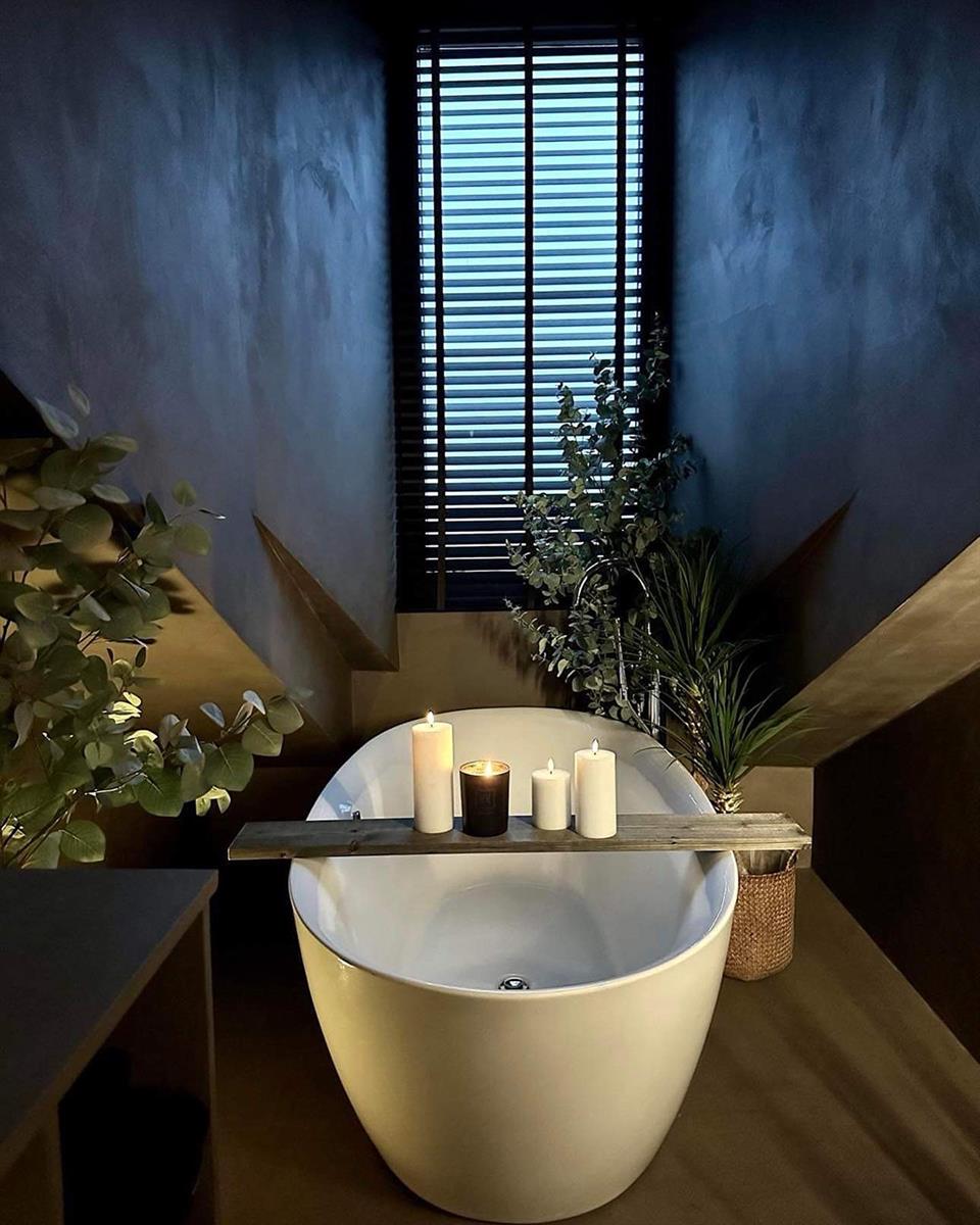 Halvor Bakke's bad med mørke vegger og trepersienner, hvitt badekar og grønne planter. Foto.